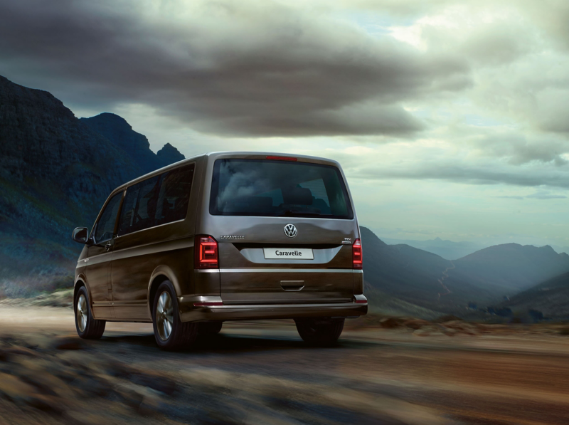 A Volkswagen van for families, the Caravelle driving away into the mountains on an overcast day.