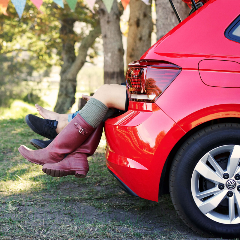 Boots hanging down from the back of the a red Volkswagen Polo at a festival.