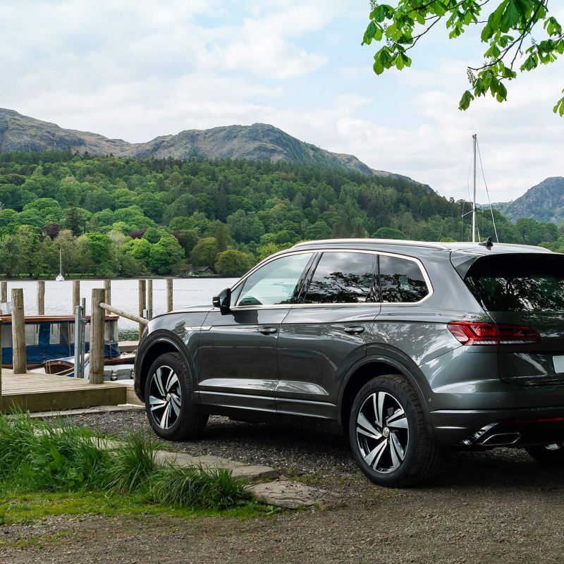 A grey Volkswagen Touareg parked in the mountains near a lake.