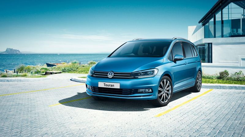 A blue Volkswagen Touran parked in front of a building near the sea
