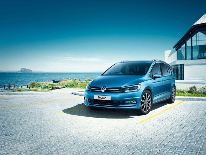 A blue Volkswagen Touran parked in front of a house near the sea