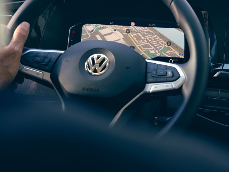 Une main contrôle le volant, l’écran affiche la carte d’un système de navigation.