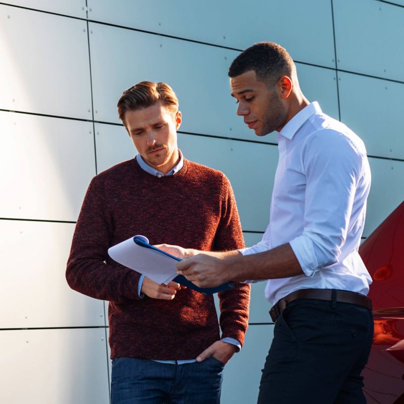 Two men looking at a chart next to a car