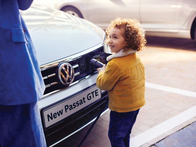 A young child connecting a plug to the front of a Volkswagen Passat GTE.