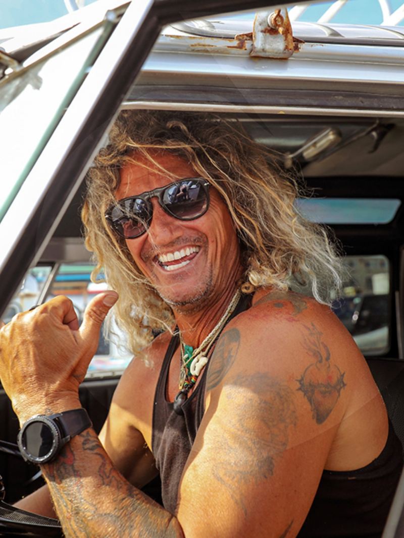 Surfer Martin sitzt am Steuer seines Californias und grüßt uns lächelnd.
