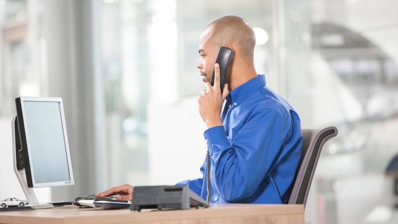 Man sat at desk on the phone, looking at his computer screen