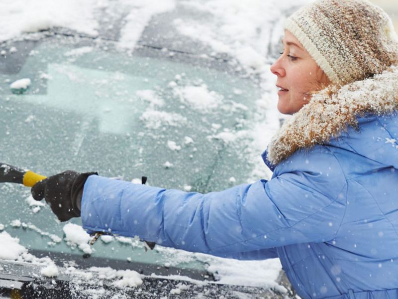 Kvinna tar bort snö från vindrutan på bil