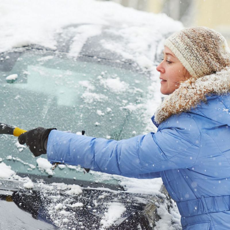 Kvinna tar bort snö från vindrutan på bil