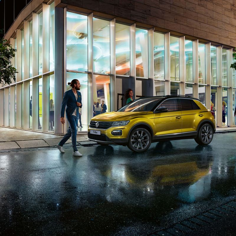 A yellow Volkswagen T-Roc parked in a well lit city street at night.