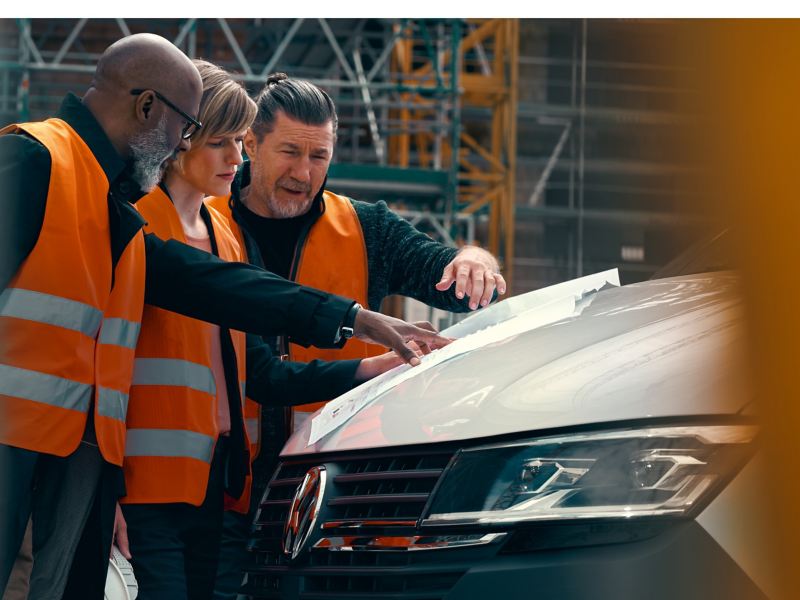 Trois personnes sur un chantier sont penchées sur un plan de construction.