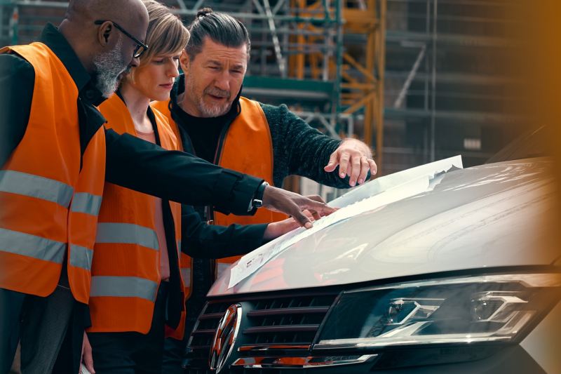 3 ouvrier, une femme et deux hommes regardant un plan sur le capot du transporter 6.1 Combi