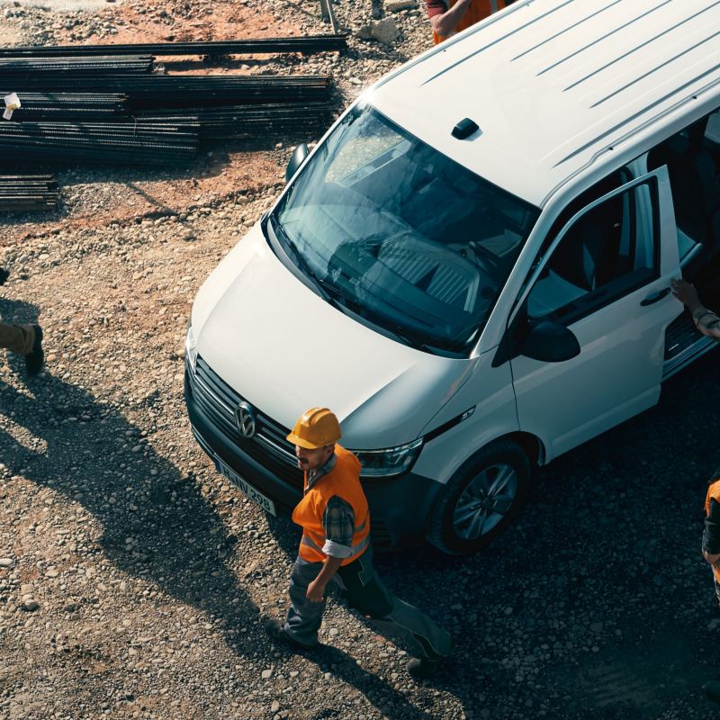 Einige Bauarbeiter stehen auf einer Baustelle um ihren Volkswagen Transporter 6.1 Kombi.