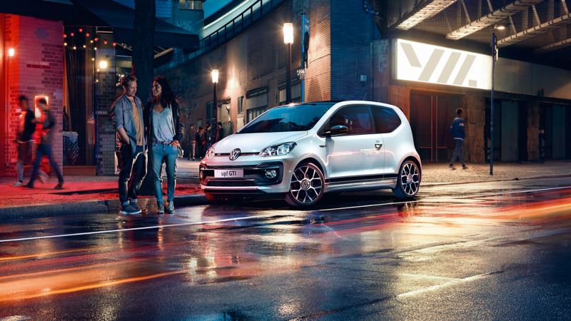 A white Volkswagen up! GTI parked on a well-lit city street at night.