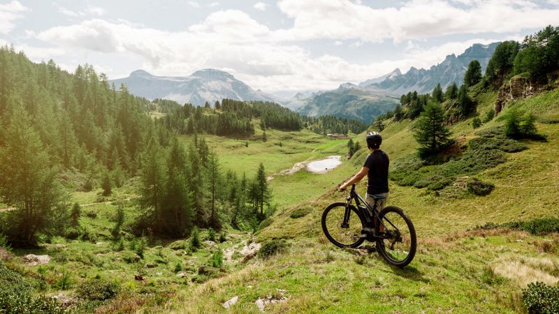Hombre joven en bicicleta mirando un paisaje de montaña desde la altura