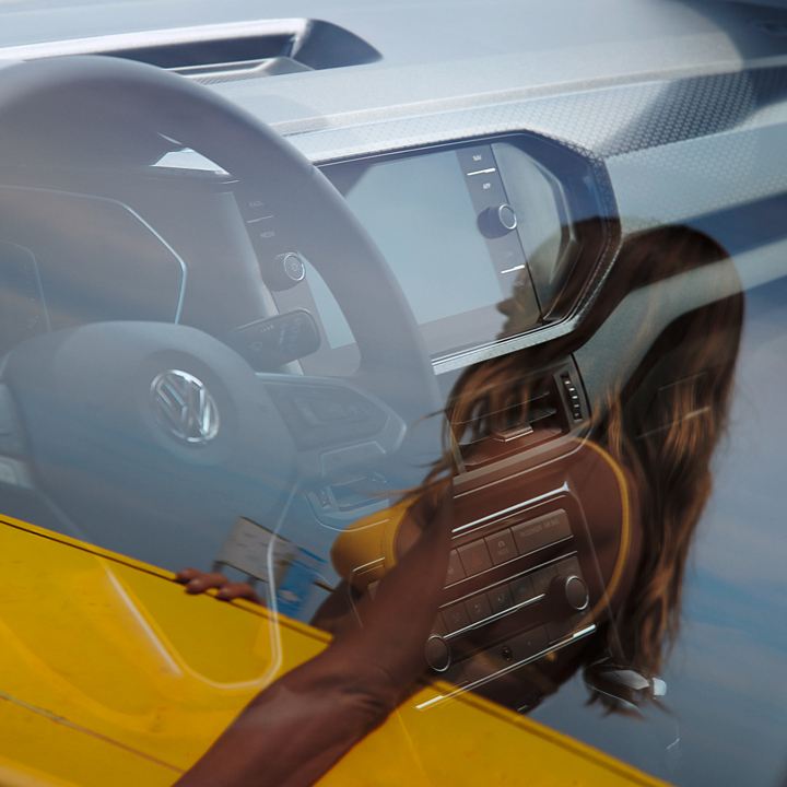 Reflejo de una chica con una tabla de surf amarilla sobre el cristal de un Volkswagen