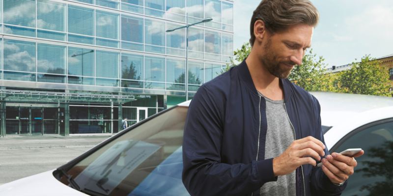 Detalle de las manos de un hombre usando en móvil y apoyado en un Volkswagen azul