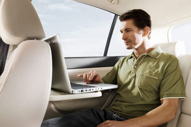 A man using his laptop on a foldout table in the back passenger seat of a Volkswagen Golf.
