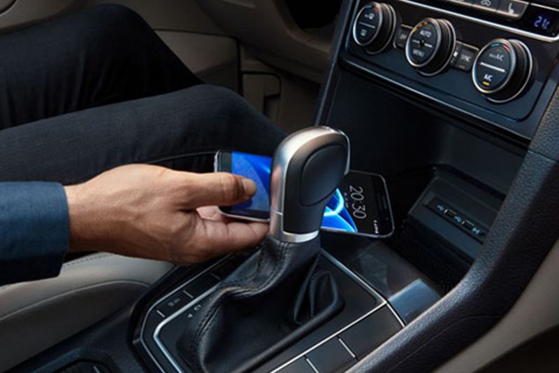 Person placing their phone in the dashboard compartment of a Volkswagen Golf.