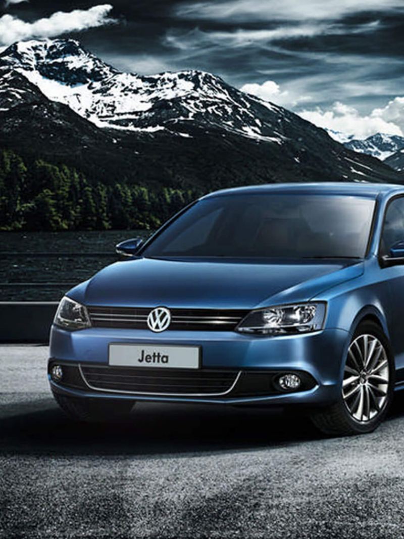 A blue Volkswagen Jetta surrounded by snow covered mountains.