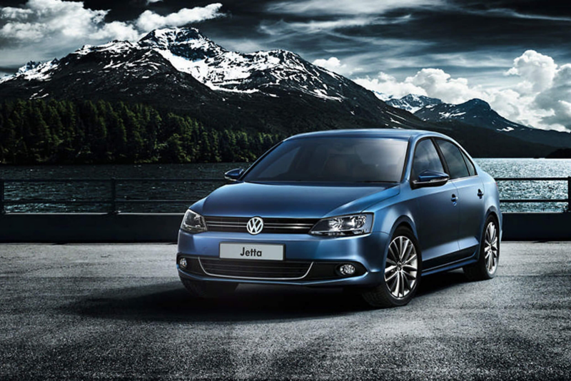 A blue Volkswagen Jetta surrounded by snow covered mountains.