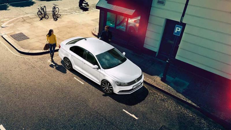 Ariel shot of a white Volkswagen Jetta, with a lady approaching.
