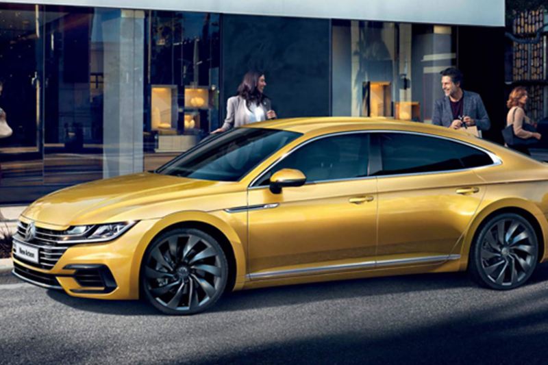 A yellow Volkswagen Golf R-Line, on a shopping street with pedestrians.