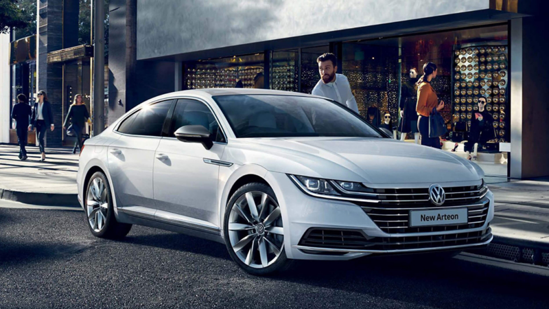 A white Volkswagen Arteon parked on a city street outside of shops, the owner getting in.