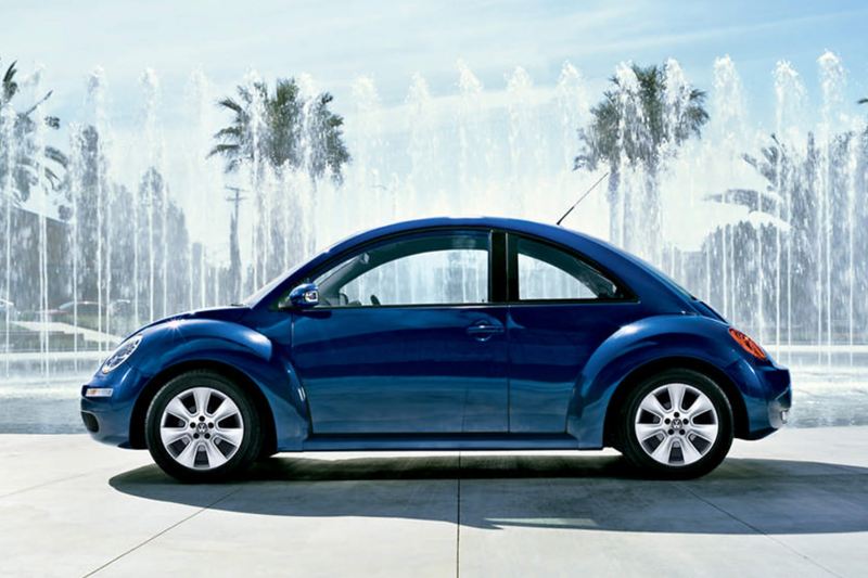 Profile shot of a blue Volkswagen Beetle, fountains and tree's in the background.