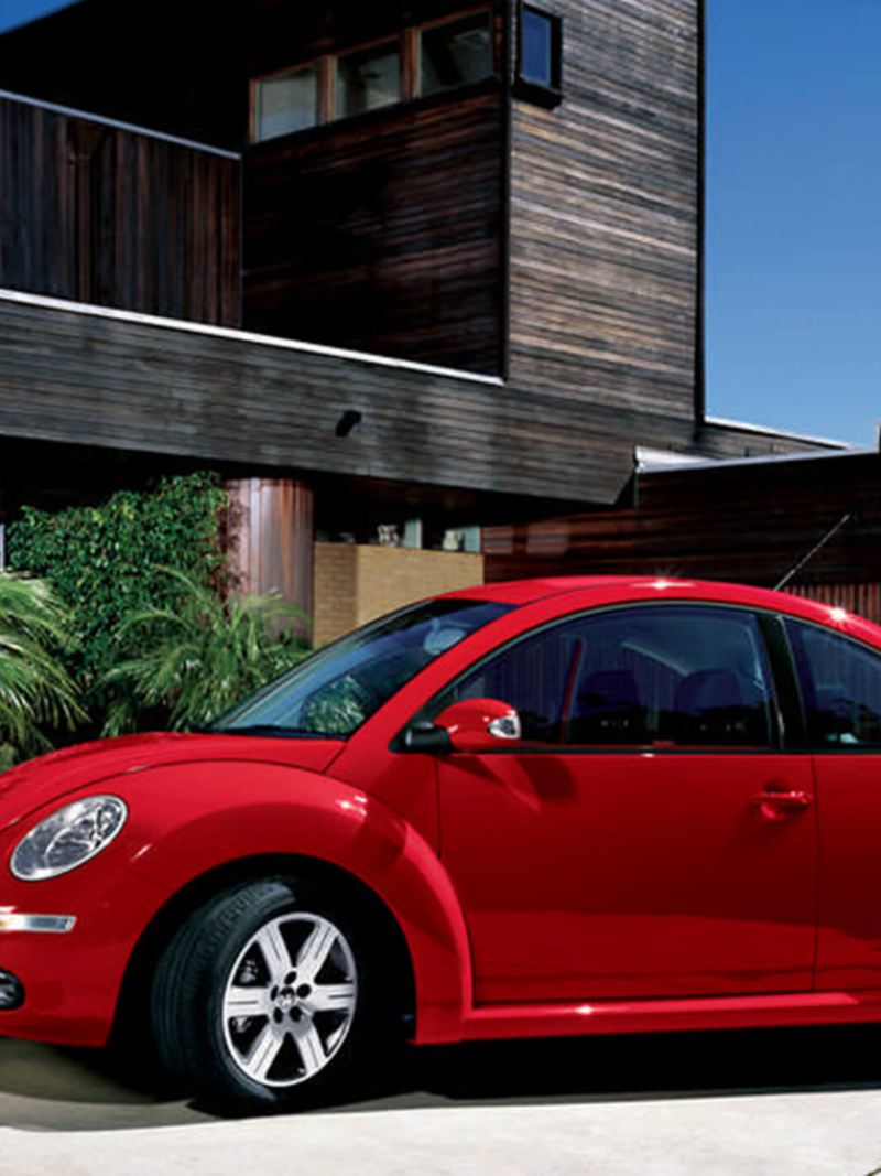A red Volkswagen Beetle, outside a wooden-clad building, on a coastline.
