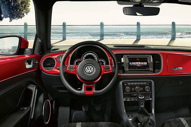 Interior dashboard shot of a Volkswagen Beetle, the see visible through the windscreen.