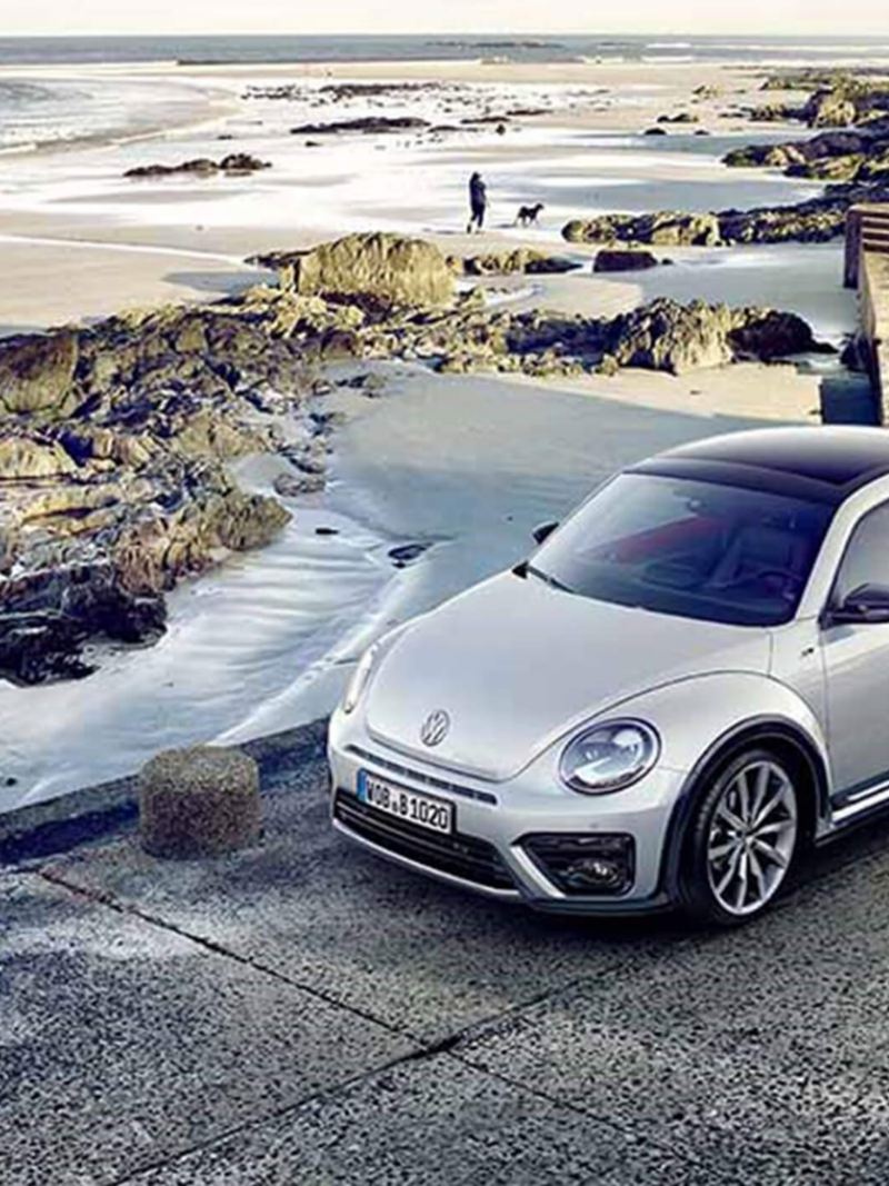 A white Volkswagen Beetle, on a rocky coastal road.