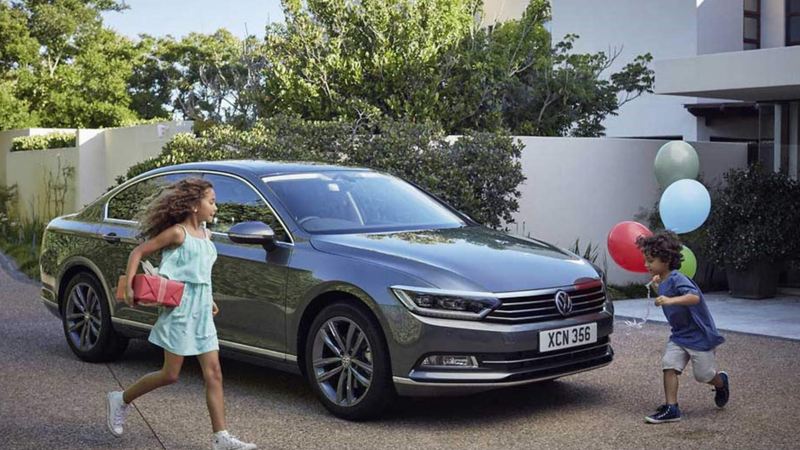 Two children playing around a Volkswagen Passat, outside their family home.