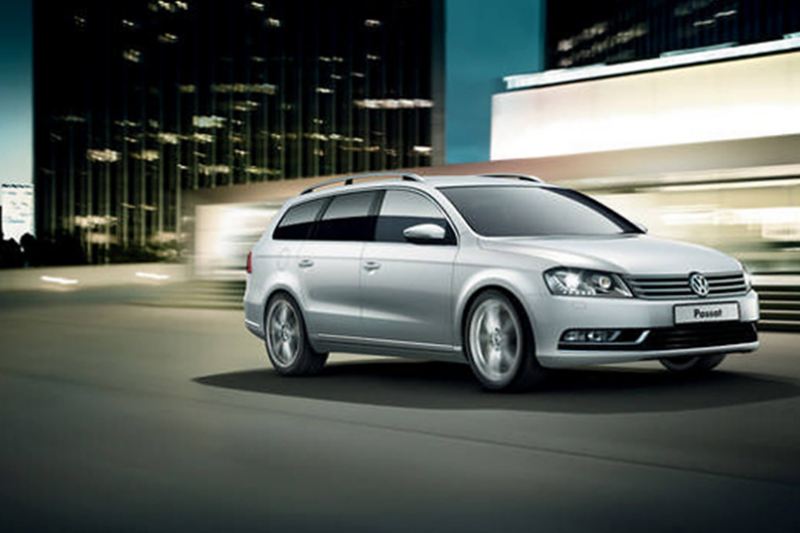 A silver Volkswagen Passat Estate driving through the city at night.