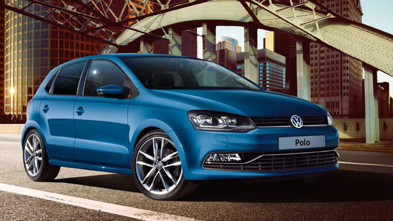 A blue Volkswagen Polo, under a steel structure, in a city setting,