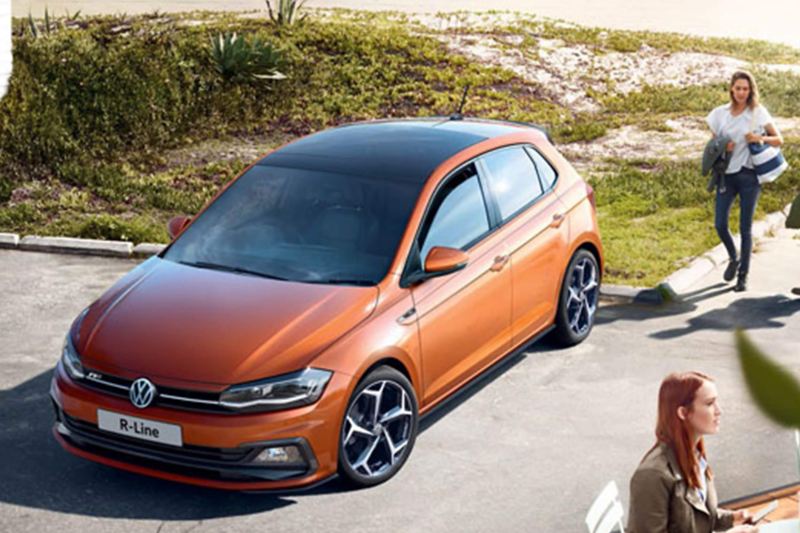 Orange Volkswagen Polo driving along a coastal road.