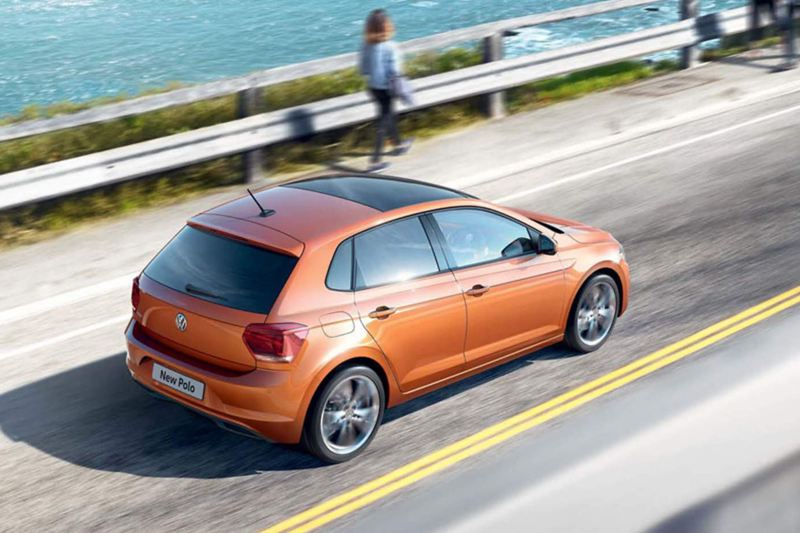 Orange Volkswagen Polo driving along a coastal road.