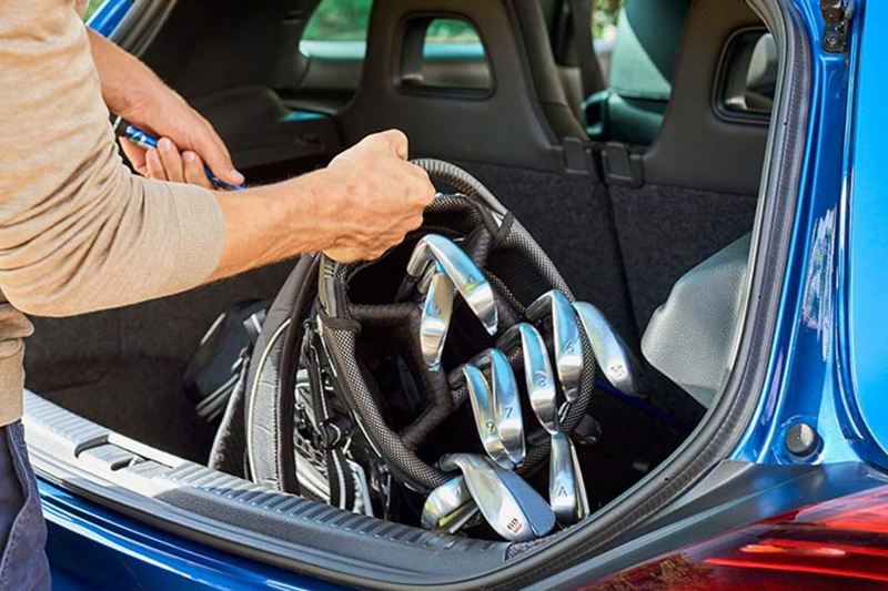 Man putting golf clubs into the boot of his Volkswagen Scirocco.