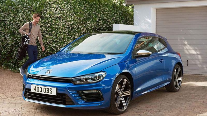 A man walking towards a parked blue Scirocco