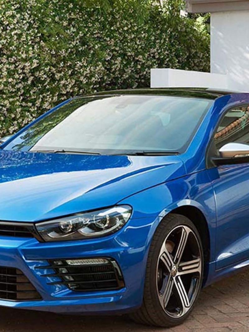 A man approaching his blue Volkswagen Scirocco, in his drive.