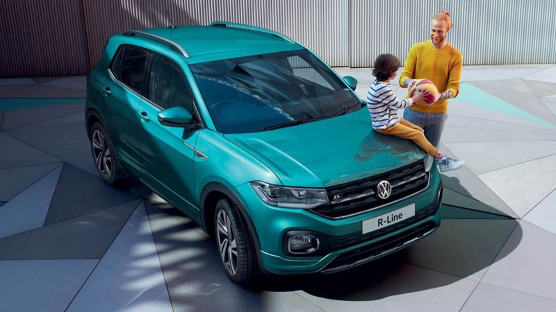 A child sitting on the bonnet of a T-Cross while his father watches