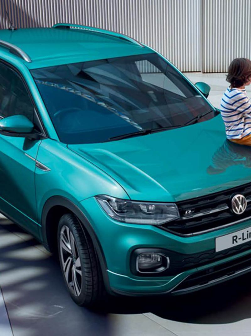 Young child sat on top of a green Volkswagen T-Cross, with her father.