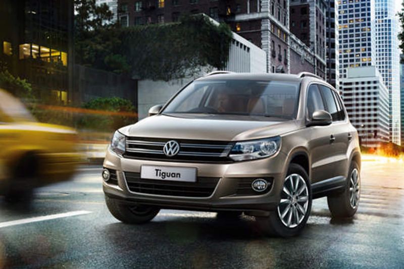 A bronze Volkswagen Tiguan, driving through a city in the evening.