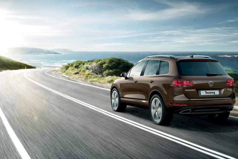 Bronze Volkswagen Touareg, rear shot, on a coastal road.