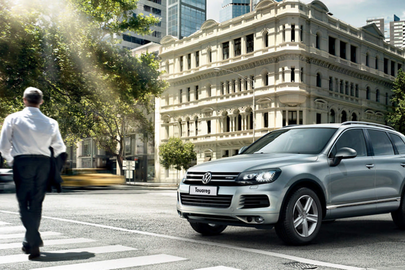 Man walking on a zebra crossing whilst a silver Volkswagen Touareg waits.