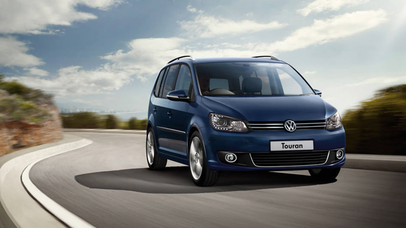 Blue Volkswagen Touran, driving on a bendy coastal road.