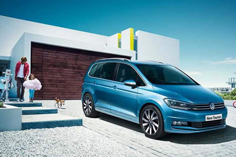 Family and dog with approaching a blue Volkswagen Touran.