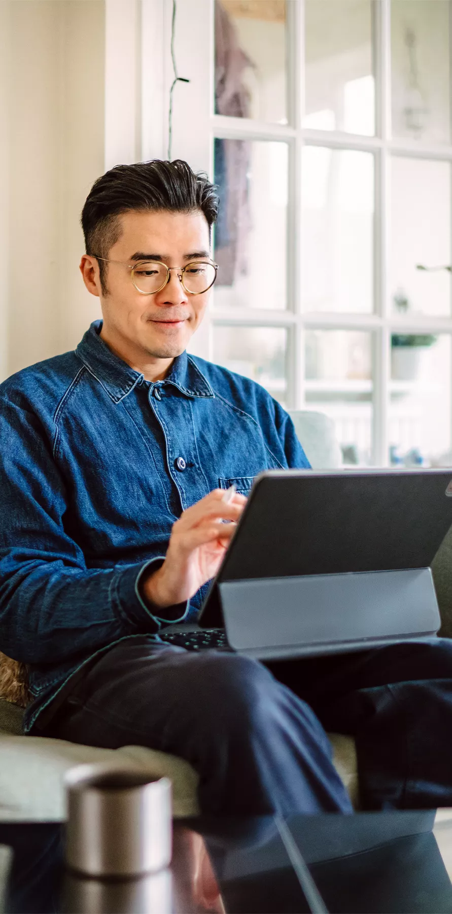 Mann im blauen Hemd sitzt auf dem Sofa und arbeitet an seinem Tablet