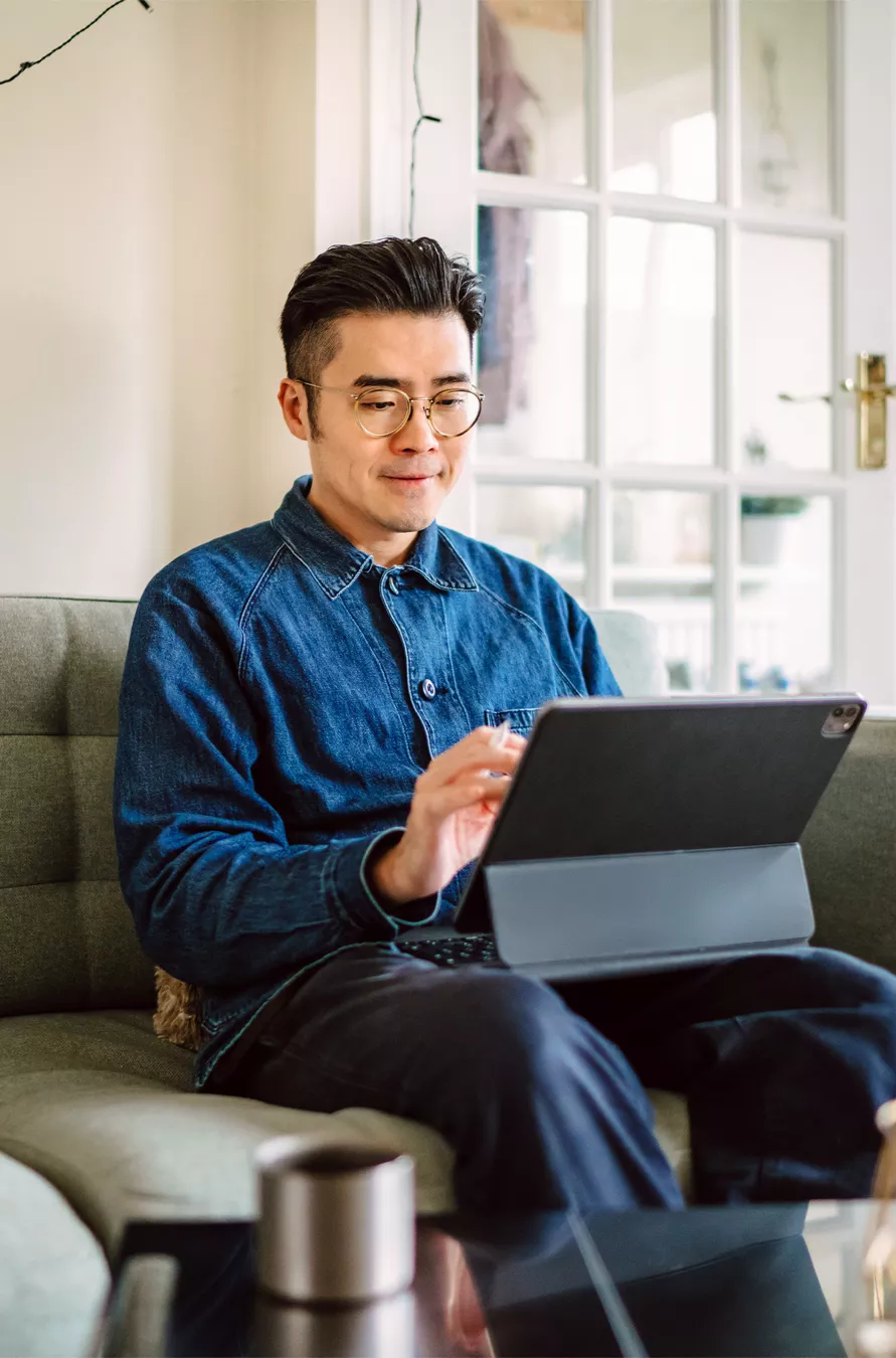 Mann im blauen Hemd sitzt auf dem Sofa und arbeitet an seinem Tablet