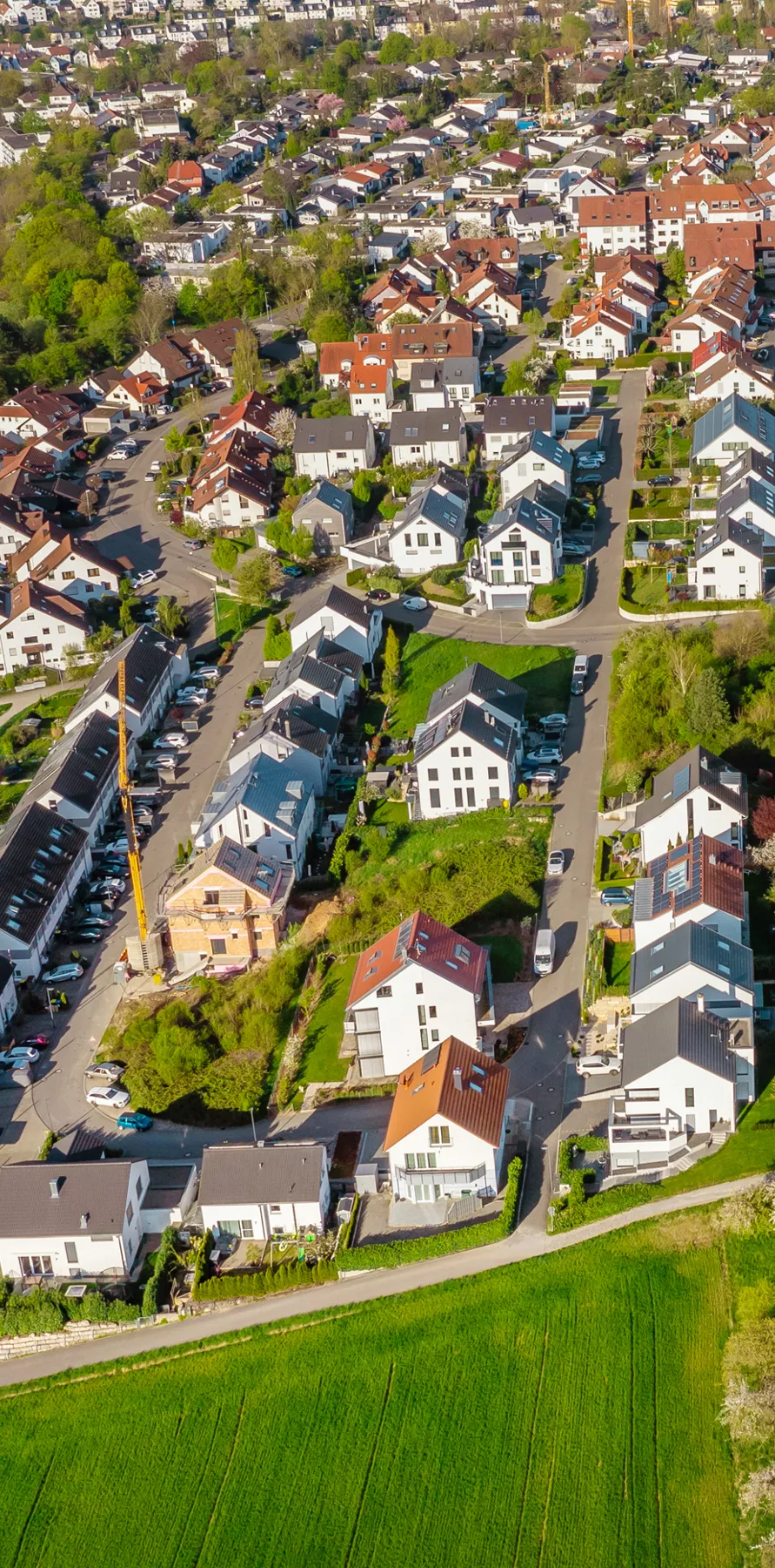 Luftaufnahme eines Wohngebiets mit Reihenhäusern, Straßen und grünen Feldern daneben.