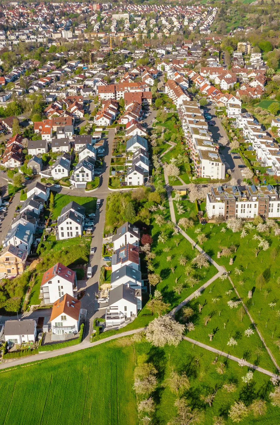 Luftaufnahme eines Wohngebiets mit Reihenhäusern, Straßen und grünen Feldern daneben.